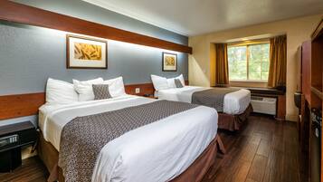 Une chambre d’hôtel avec deux lits, une fenêtre avec des rideaux, un radiateur et des œuvres d’art accrochées aux murs.