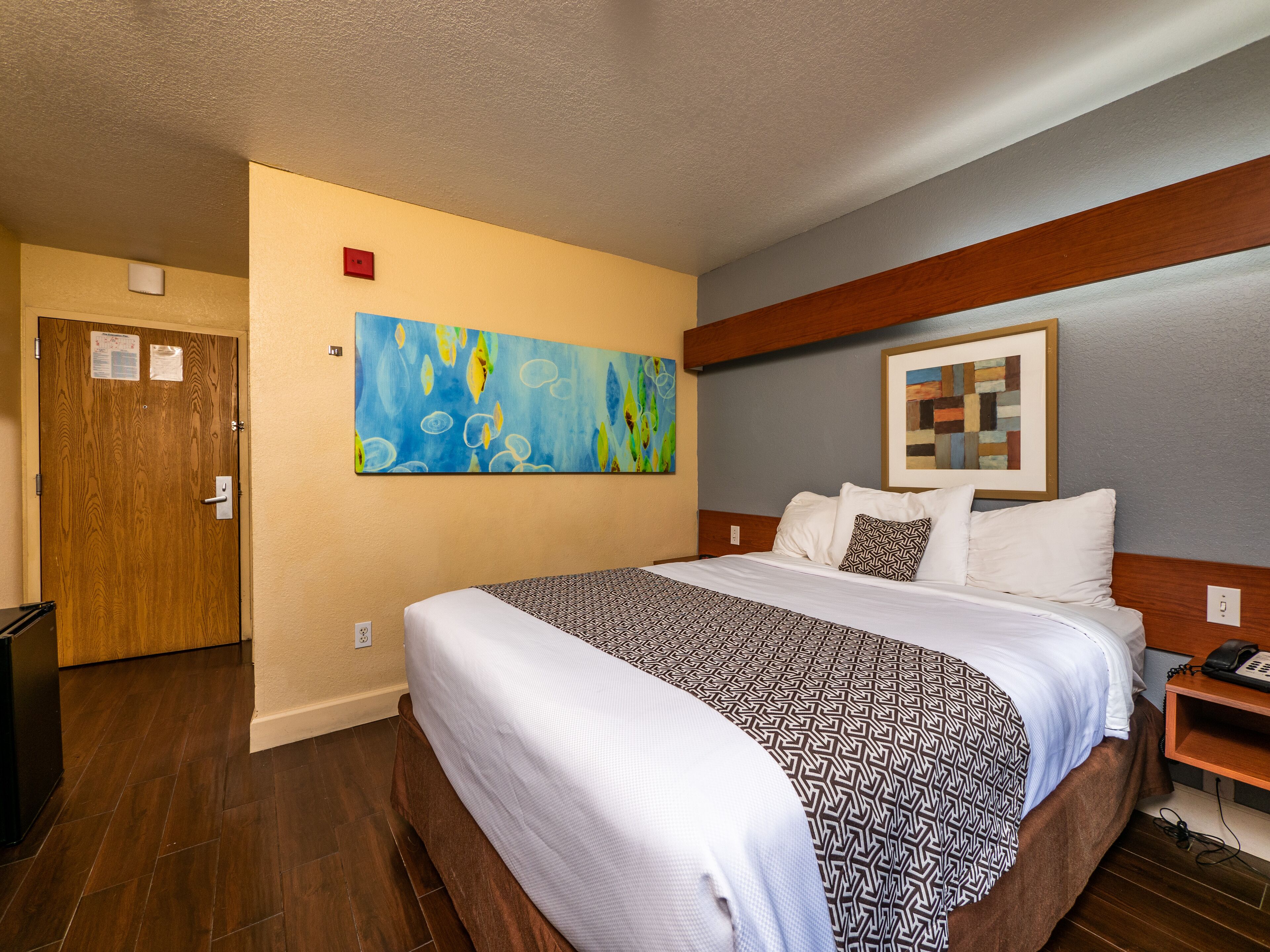 A hotel room with a large bed, a wooden headboard, a painting on the wall, and a wooden door.