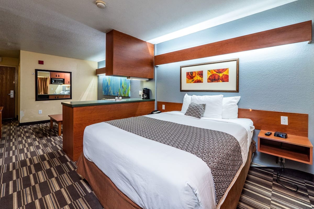 A hotel room with a large bed, a small desk, a microwave, a sink, and artwork on the walls.