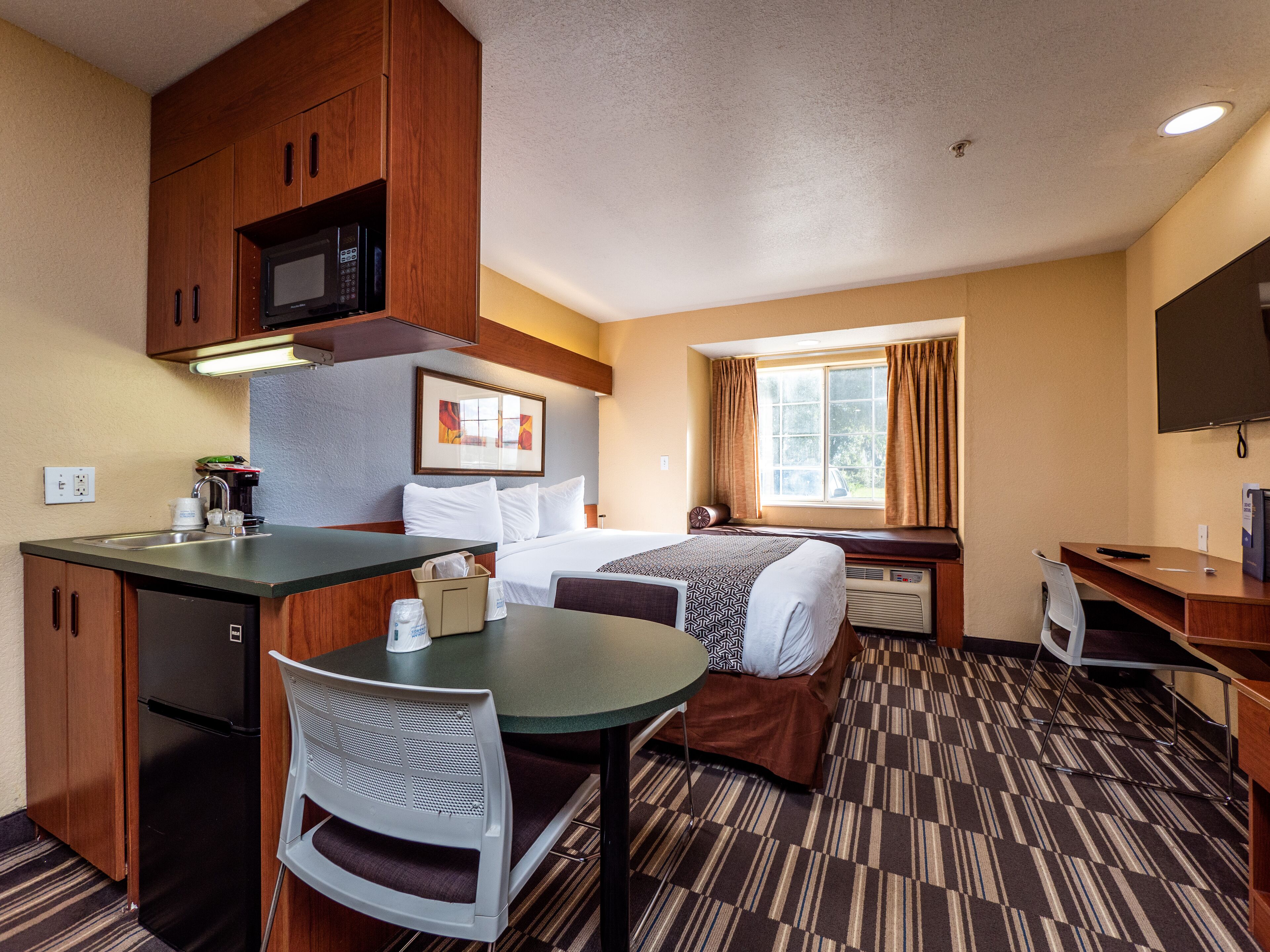 Una habitación de hotel con kitchenette, una cama, un escritorio y un ventanal con cortinas.