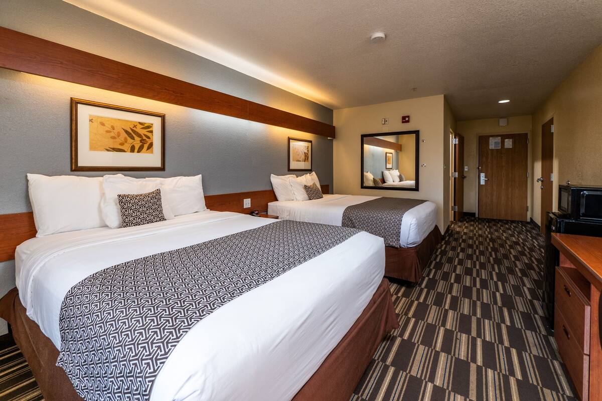 A hotel room with two beds, a wooden headboard, a large mirror, and a television.
