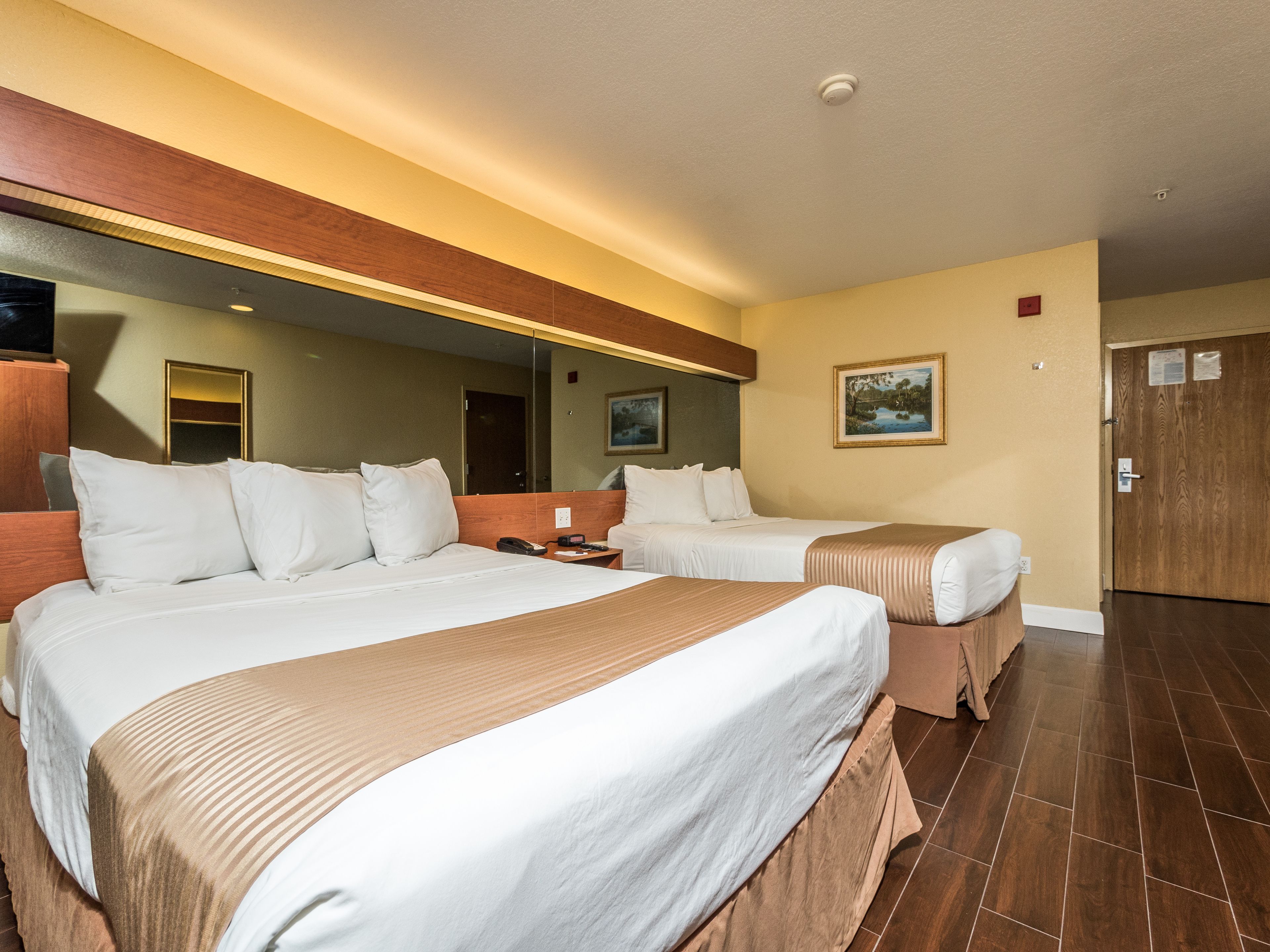 A hotel room with two beds, a large mirror, a painting on the wall, and a wooden door.