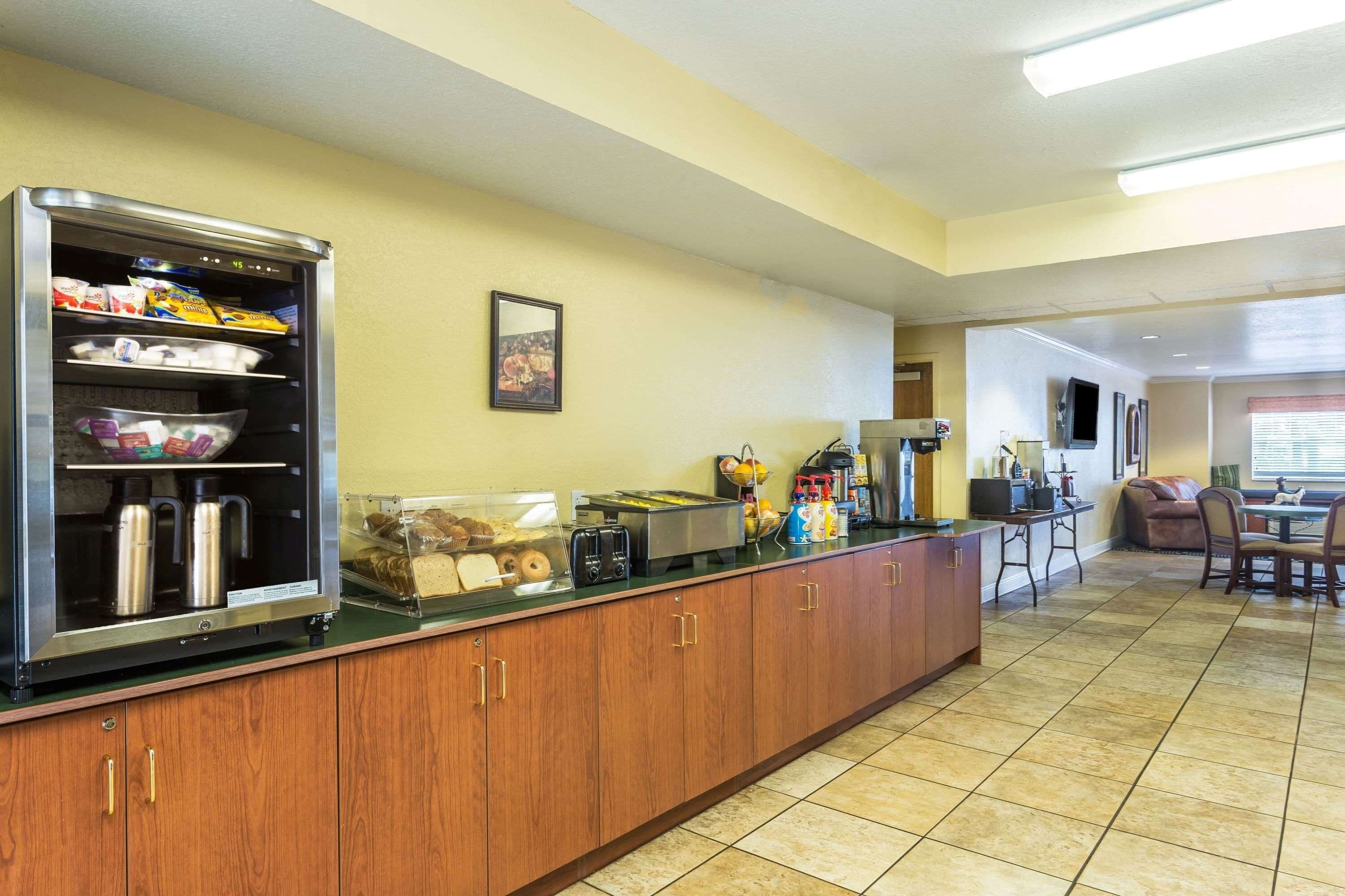 A kitchen area with a refrigerator, microwave, toaster, and coffee machine. There is a counter with various food items and a seating area with a table and chairs.