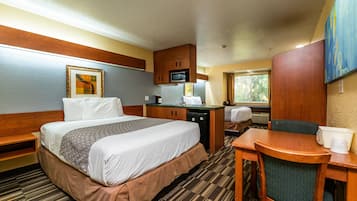 A hotel room with a bed, a desk, a chair, a microwave, and a television.