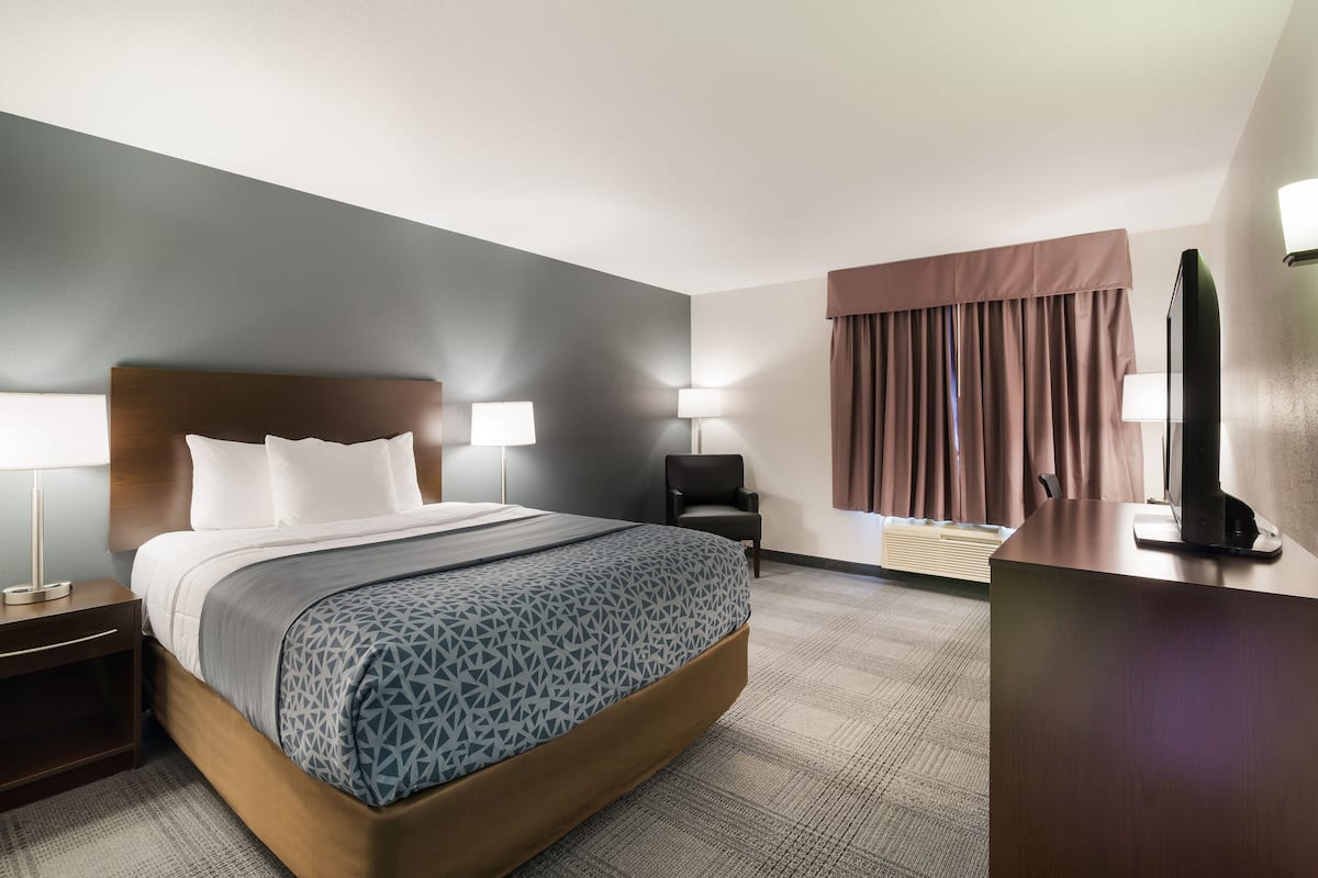 A hotel room with a bed, bedside lamps, a desk, a chair, and a television.