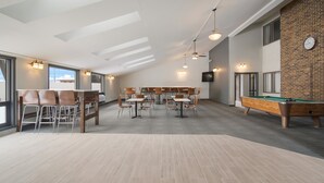 A spacious indoor area with a pool table, multiple tables and chairs, and a brick wall. - Econo Lodge Williston (Williston)