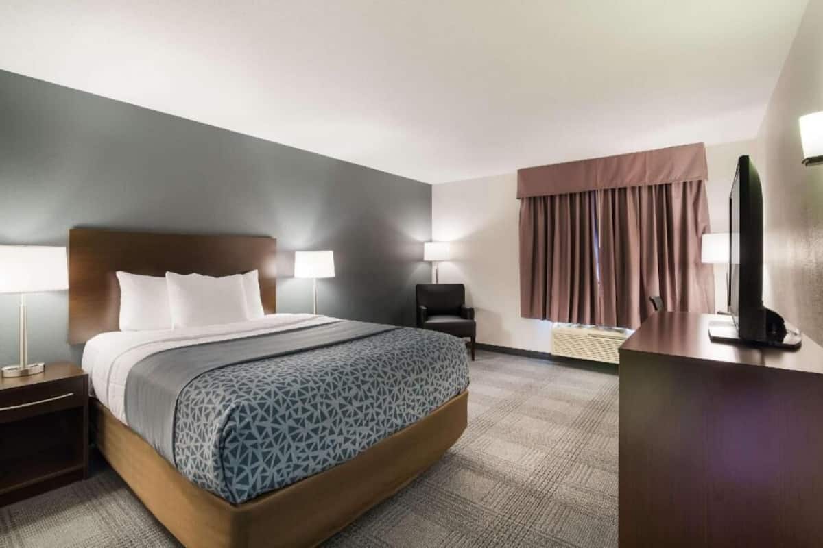 A hotel room with a bed, bedside tables, lamps, a desk, and a chair.