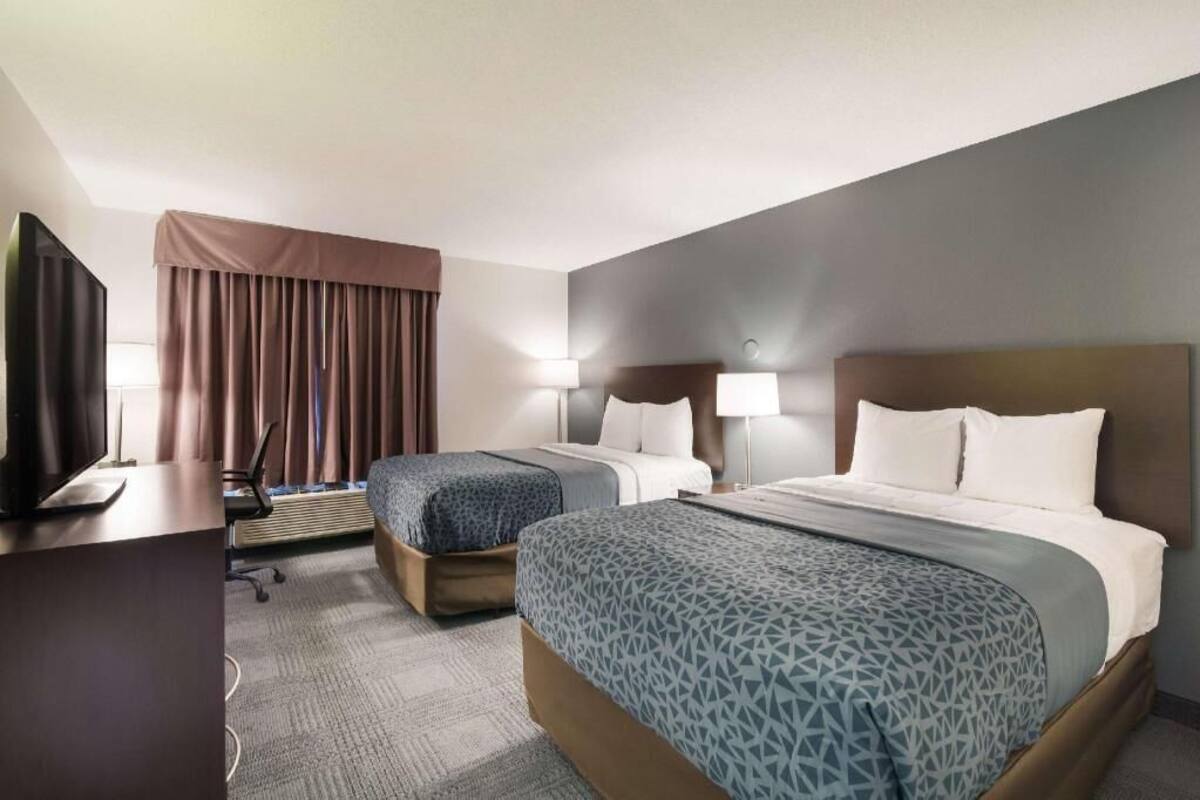 A hotel room with two beds, a desk, a TV, and a window with curtains.