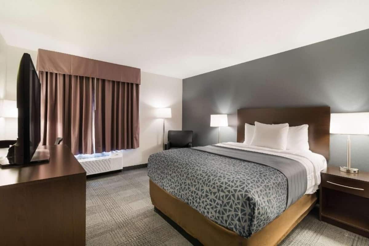 A hotel room with a bed, bedside lamps, a desk, a chair, and a TV.