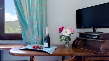 Ein Holztisch mit einer Weinflasche, einer Schale Erdbeeren und einer Blumenvase. Ein Fernseher befindet sich rechts neben dem Tisch.