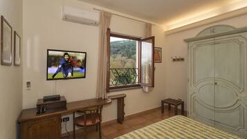 Un dormitorio con cama, escritorio con silla, televisor, armario y ventana con cortinas.
