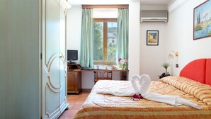 Een hotelkamer met een bed, een bureau, een kledingkast, een raam met gordijnen, een schilderij en een airconditioning.
