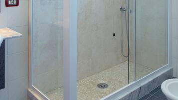 Ducha con paredes de vidrio, piso de baldosas y panel de control en la pared.