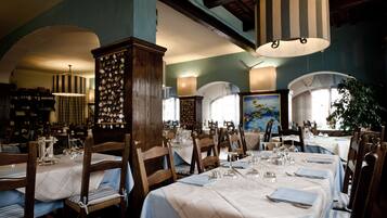 A dining area with tables set for service, wooden chairs, and hanging lamps.