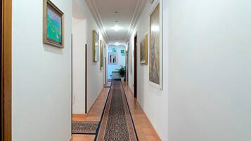 Un couloir aux murs ornés de tableaux encadrés, avec un tapis à motifs et un sol carrelé.
