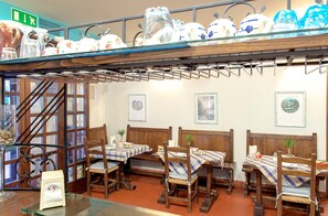 A dining area with wooden tables and benches, a staircase, and a display of ceramic dishes on the wall. - Hotel Da Carlos (Lucca)
