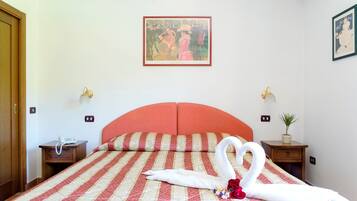 Una camera d'albergo con un letto, un telefono su un comodino, una lampada a parete, un quadro incorniciato e una pianta in vaso.
