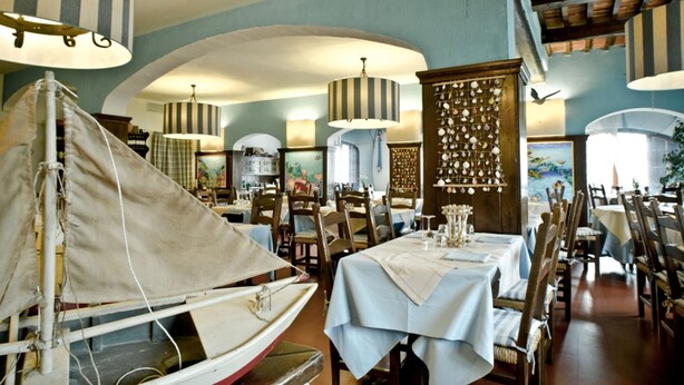 Een restaurant met gedekte tafels, een decoratie van een zeilboot en gestreepte lampen.