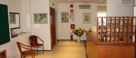 A reception area with a wooden reception desk, two wooden chairs, a vase with sunflowers, and framed pictures on the walls.