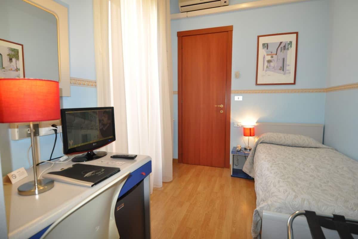 A hotel room with a desk, computer, bed, and a door.