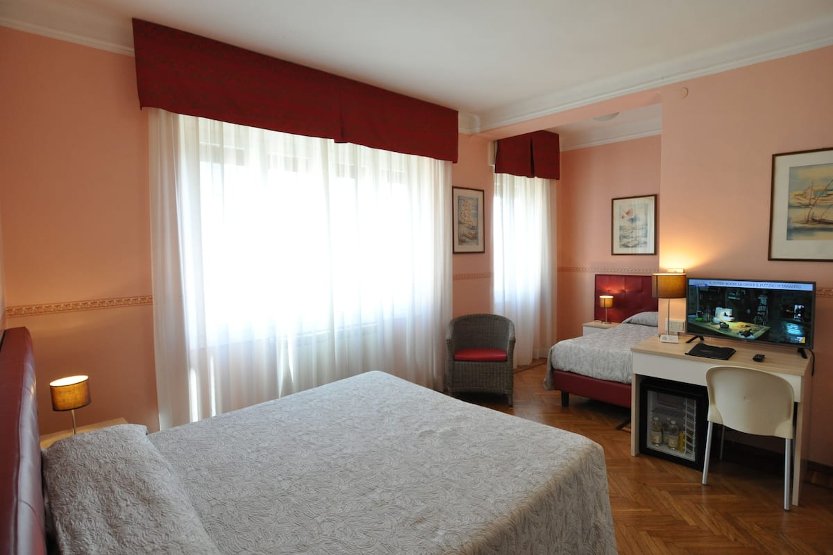 A hotel room with two beds, a desk with a computer, a chair, and a small refrigerator.