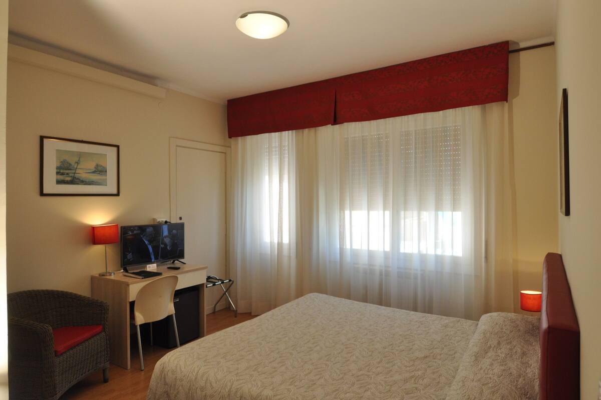 A hotel room with a bed, a desk with a computer, a chair, and a television.