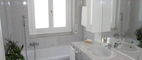 A modern bathroom with two sinks, a bathtub, and a large mirror.