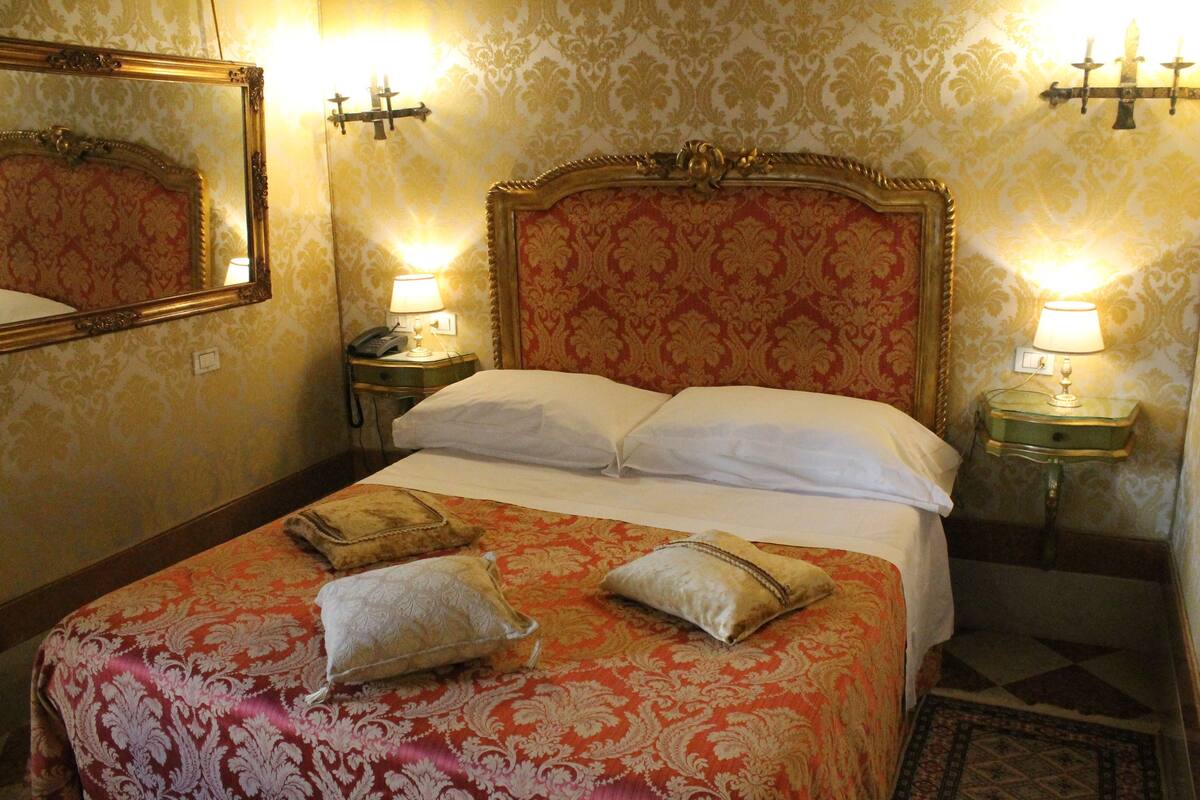 Een hotelkamer met een groot bed, twee nachtkastjes met lampen, een spiegel en behang met een patroon.