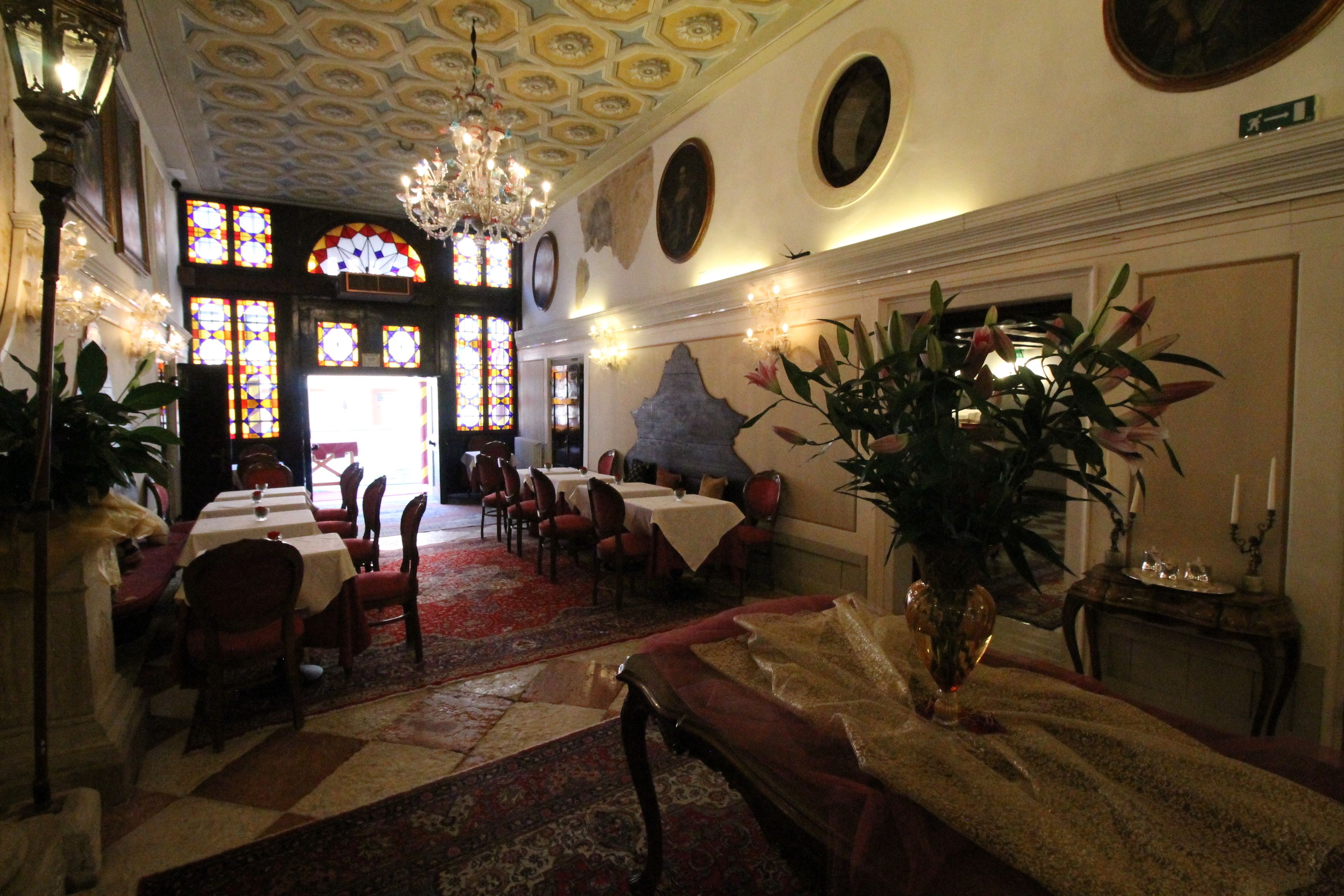 A dining area with tables and chairs, a chandelier, and a large vase with flowers.