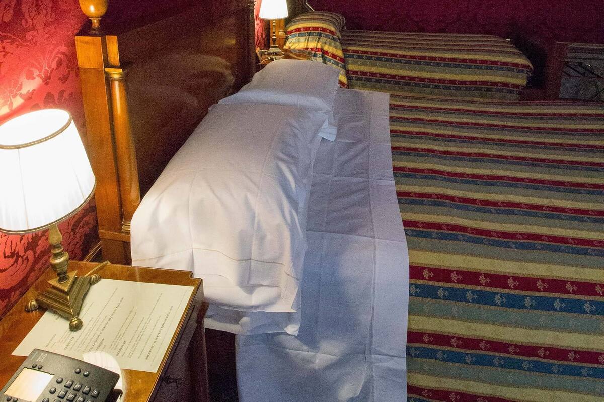 Een hotelkamer met een bed, nachtkastje met lamp, telefoon en een briefje.