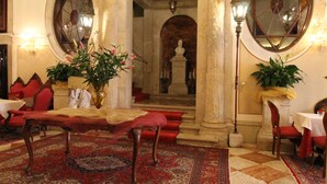 A lobby with a checkered floor, red sofas, a chandelier, and a large mirror. - Hotel Palazzo Abadessa (Venice)