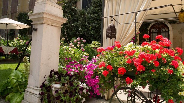 A courtyard with a statue, a bicycle planter with flowers, and a building in the background. - Hotel Palazzo Abadessa (Venice)