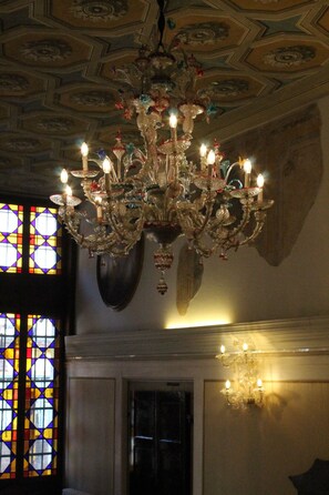 A chandelier with multiple candle-like lights, a stained glass window, and a decorative wall. - Hotel Palazzo Abadessa (Venice)