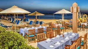 Un restaurant situé en bord de mer, avec des tables et des chaises placées sous des parasols, offrant une vue sur l’océan.