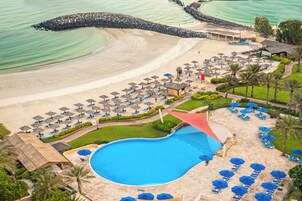 Un resort con una gran piscina, zona de playa y numerosas sombrillas y tumbonas.