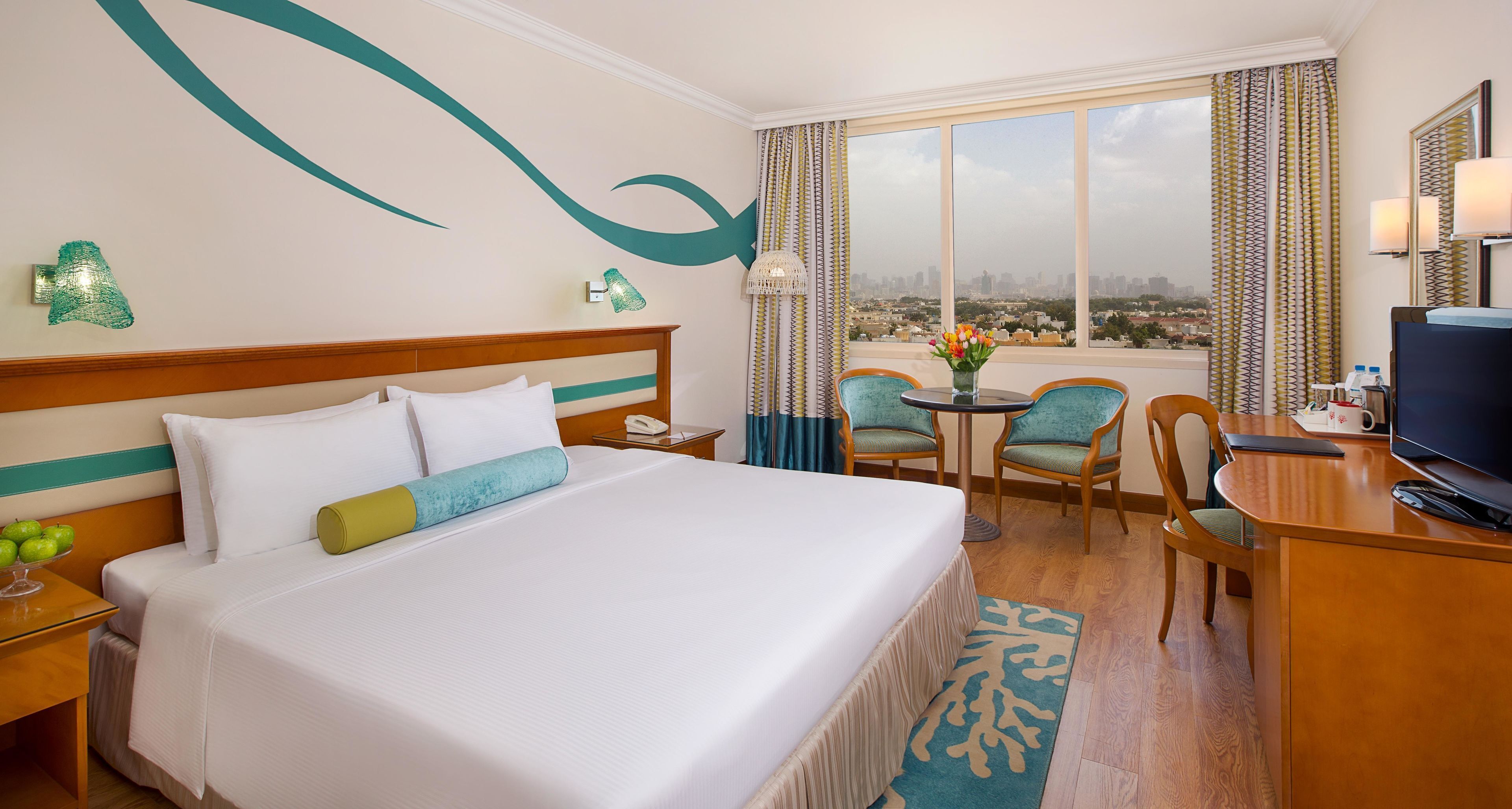 Une chambre d’hôtel avec un lit, un bureau, une chaise, une télévision et une vue sur la ville.