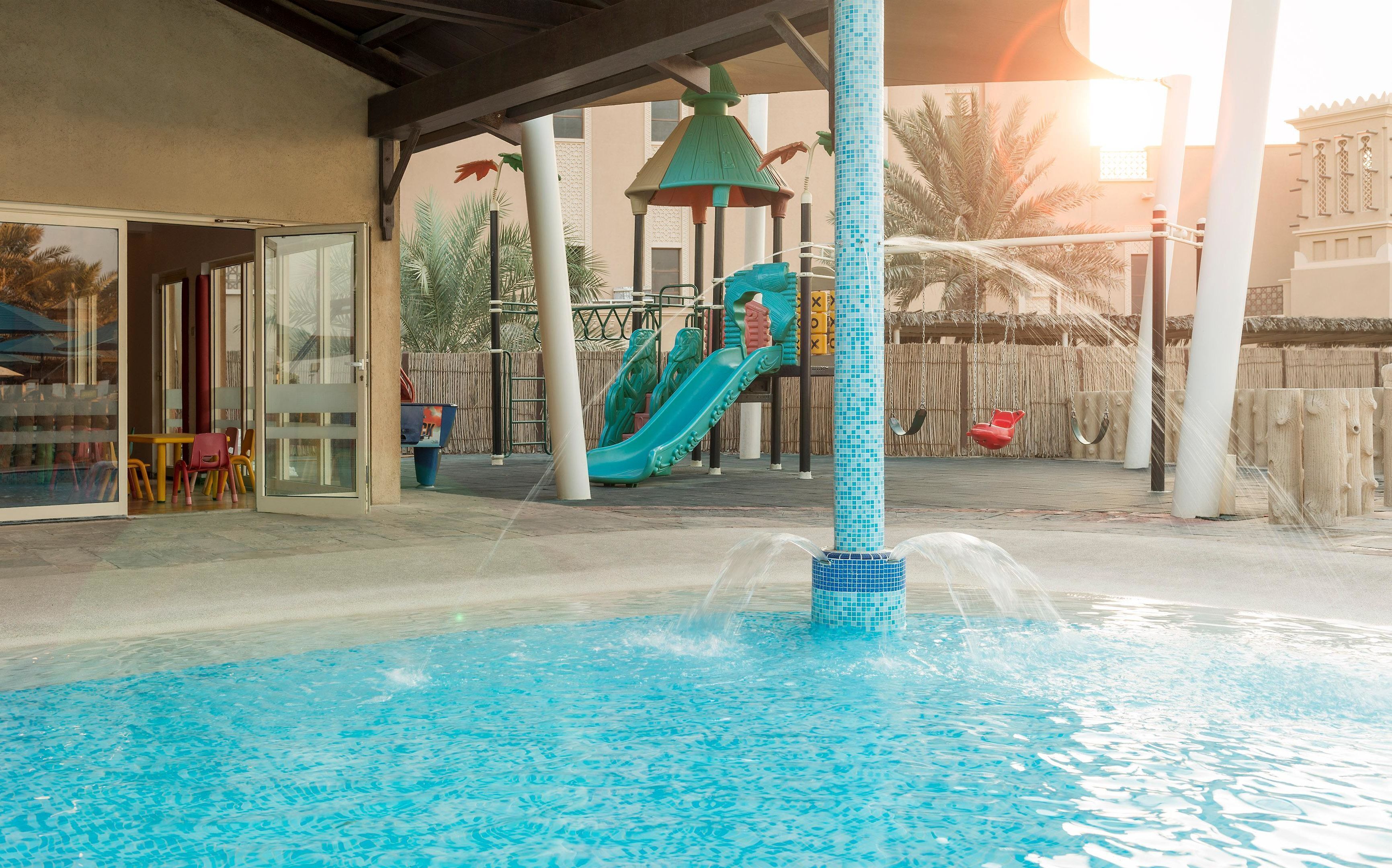 A pool area with a slide, a covered seating area, and a building with a tiled exterior.