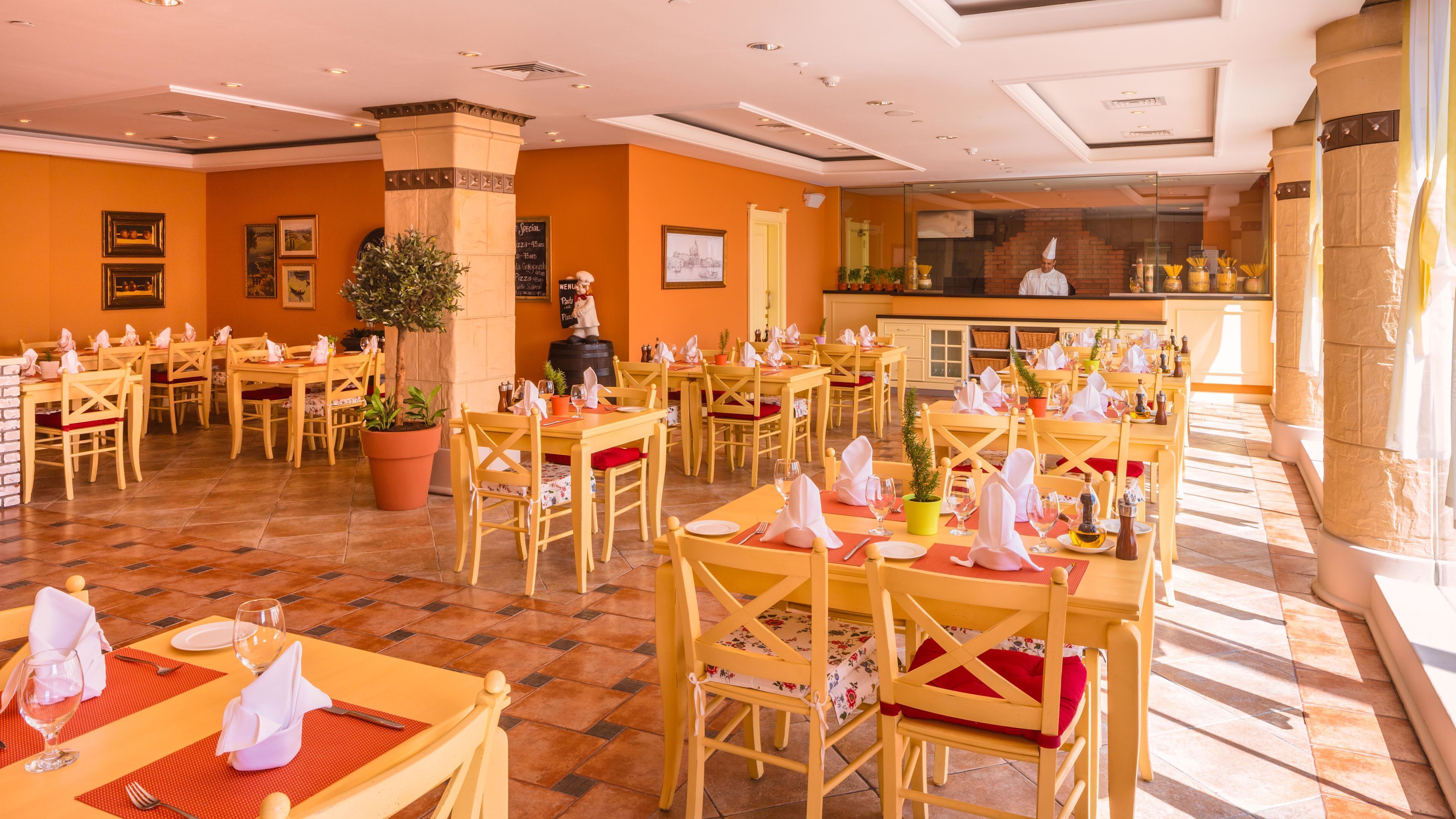 A restaurant with multiple tables, chairs, and potted plants.