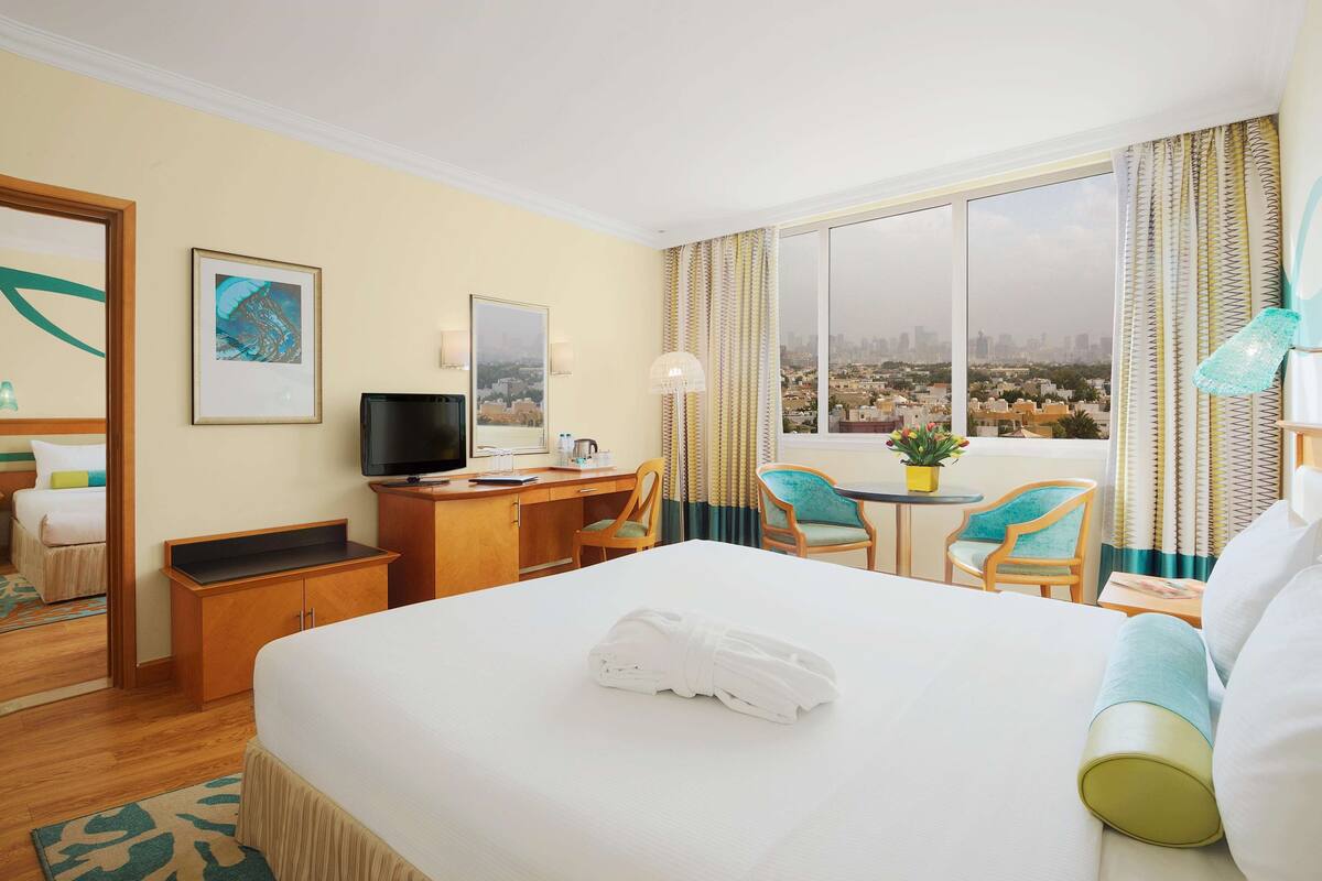 A hotel room with a bed, a desk, a TV, a chair, a small table, and a window with a city view.