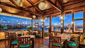 Un restaurant doté de planchers et de tables en bois, de grandes fenêtres offrant une vue sur l’océan et de lanternes traditionnelles.