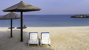 Une plage avec deux chaises longues blanches et un parasol en chaume.