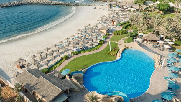 Un complexe hôtelier doté d’une grande piscine, d’une plage et de nombreux parasols.