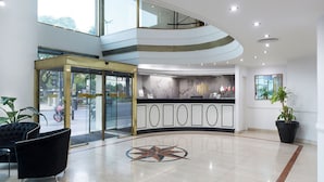 A modern hotel lobby with a curved reception desk, a central decorative floor pattern, and a glass entrance. - Imperial Park Hotel (Buenos Aires)