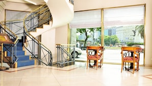 A hotel lobby with a spiral staircase, a large window offering a city view, and two wooden tables with chairs. - Imperial Park Hotel (Buenos Aires)