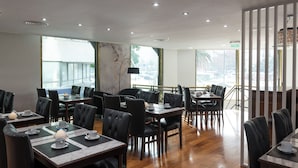 A restaurant with multiple tables and chairs, large windows, and a ceiling with recessed lighting. - Imperial Park Hotel (Buenos Aires)