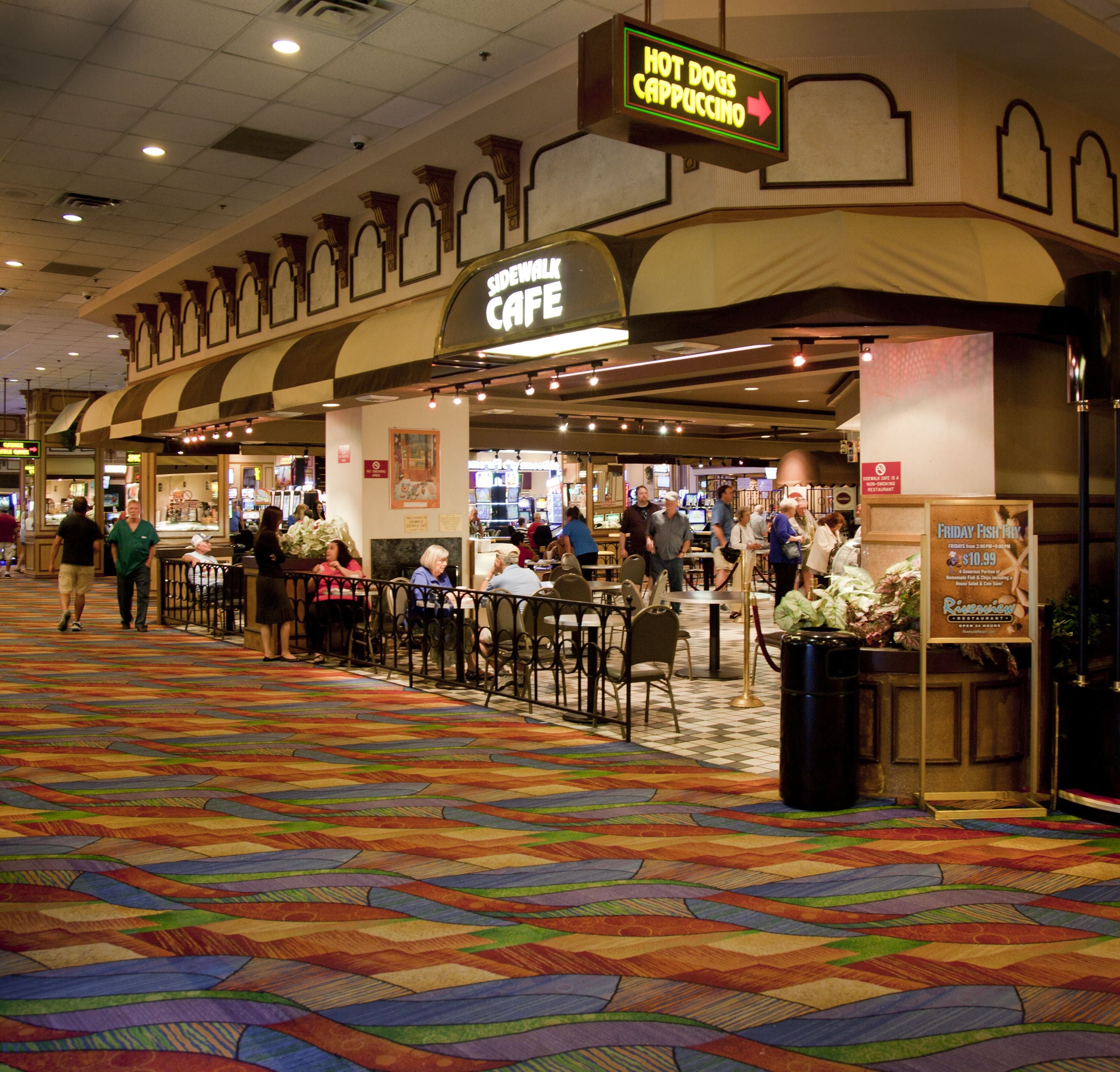 A hotel lobby with a colorful carpet, a cafe named 'Sidewalk Cafe', and a sign for 'Hot Dogs Cappuccino'.