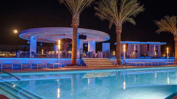 Zona de piscina con una estructura circular, palmeras y cielo nocturno.
