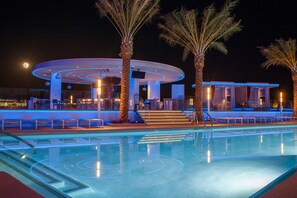 Zona de piscina con una estructura circular, palmeras y cielo nocturno.