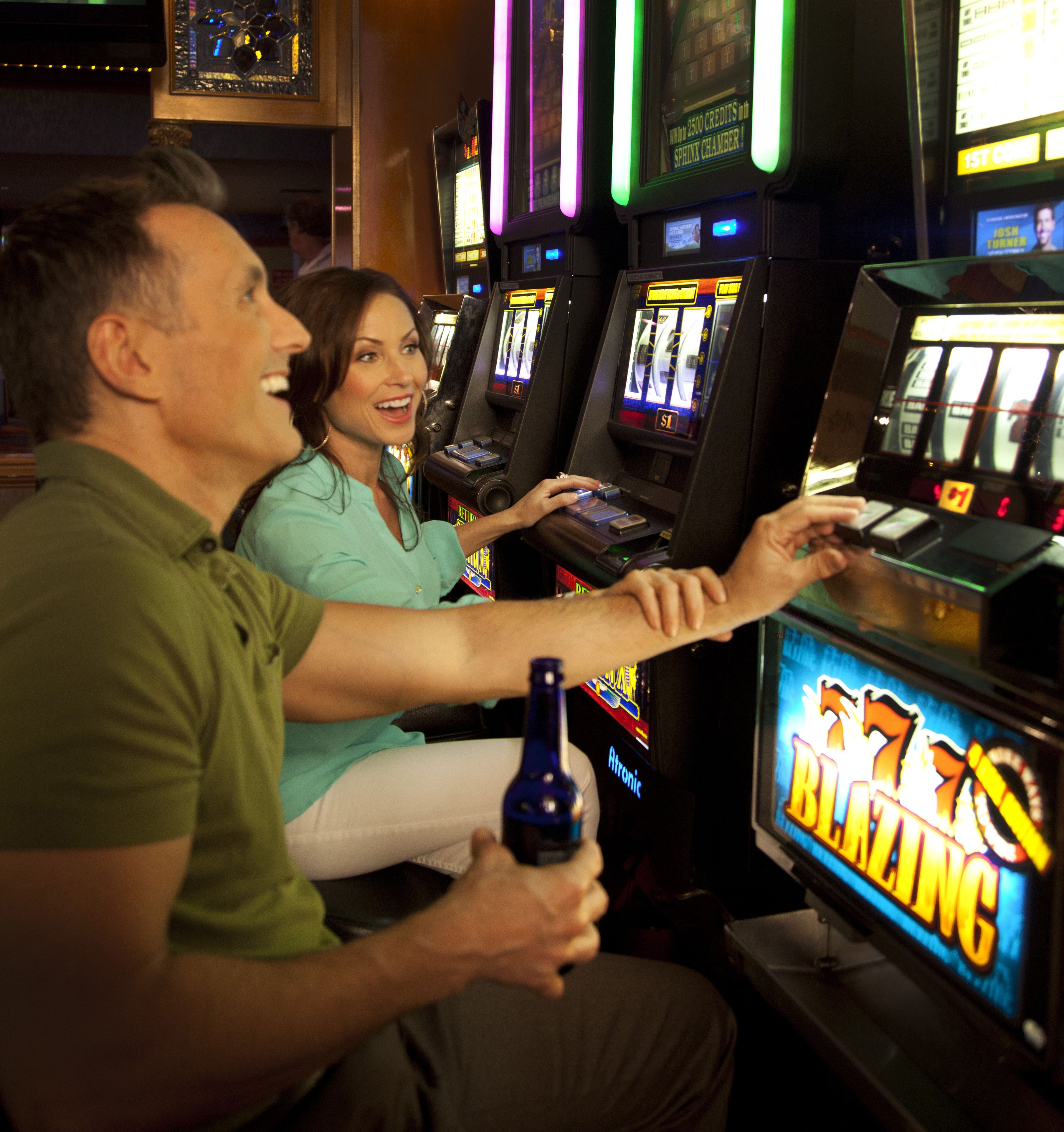 A man and a woman playing a slot machine game in a casino.