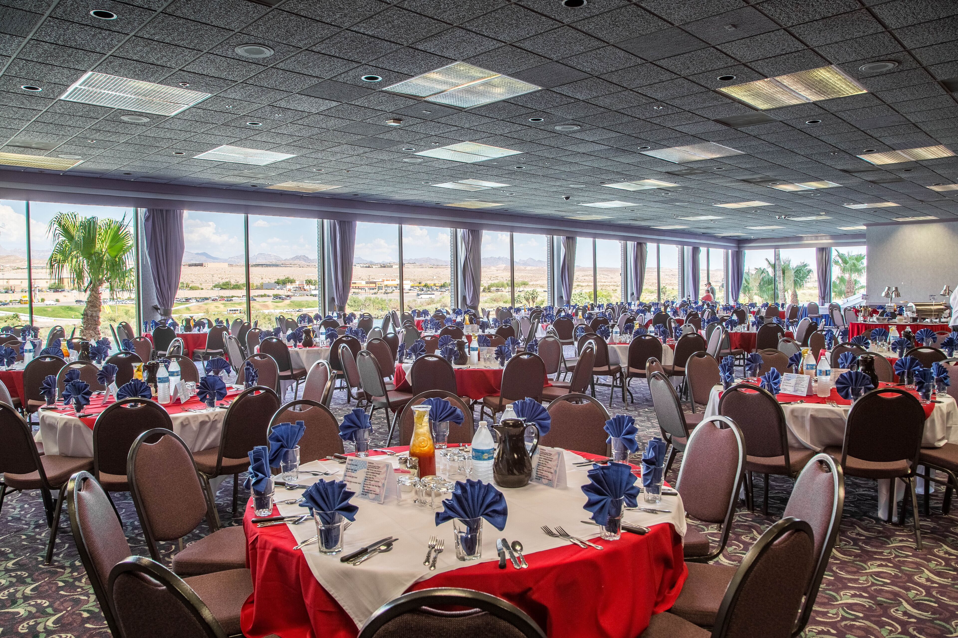 A conference room with multiple tables, chairs, and large windows offering a desert view.